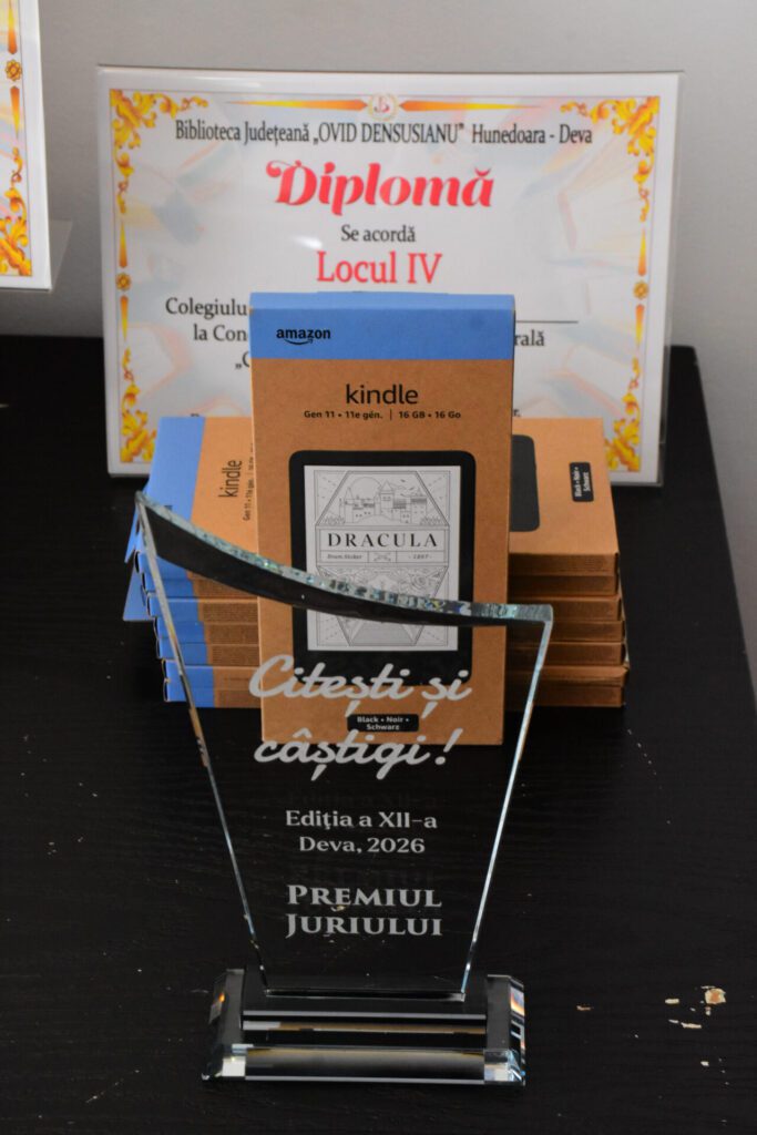 Diploma pentru locul IV la concursul "Citești și câștigi!" organizat de Biblioteca Județeană, împreună cu un dispozitiv Kindle și cărți pe un birou.