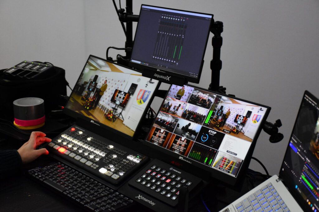 Un set de monitoare și echipamente de control pentru transmisie video, utilizat la un concurs de cultură generală.