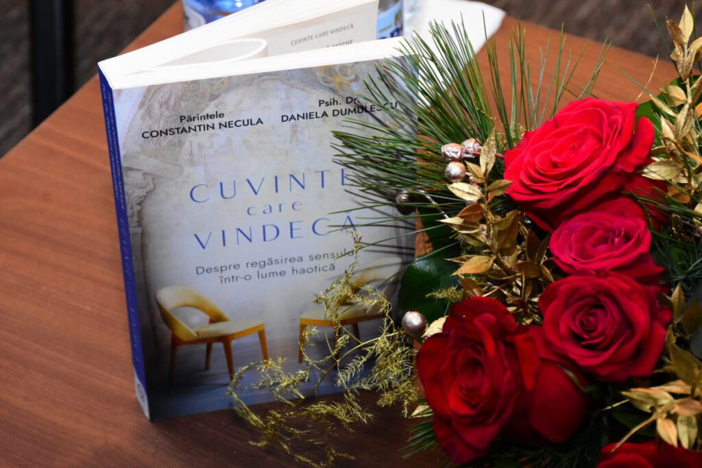 Cartea "Cuvinte care vindeca" de parintele Constantin Necula si psiholog dr. Daniela Dumulescu, prezentata pe un birou cu flori rosii, simbolizand evenimentul de lansare.
